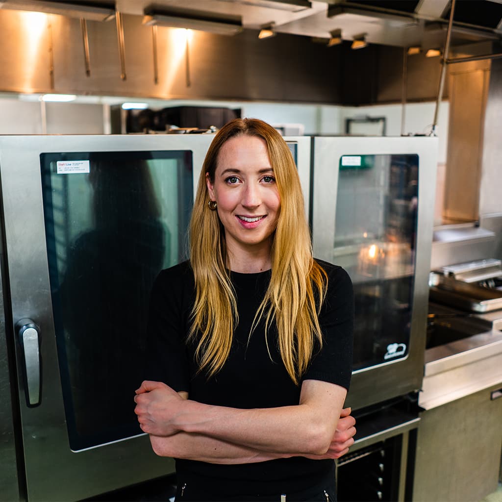 Elise Kelly standing and smiling in front of a kitchen oven.